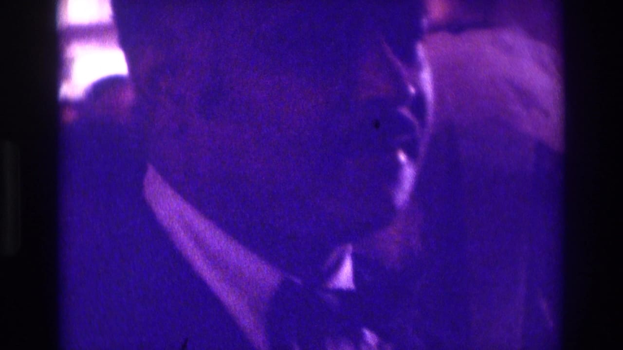1975 Atlanta home-movie frame showing a veiled bride and escort partly obscured by purple-blue ceremony lighting.