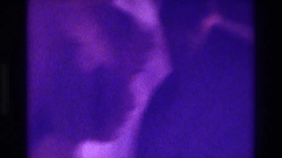 Soft 8mm frame from the 1975 Atlanta wedding showing blurred figures and a pale gown shape under purple lighting.
