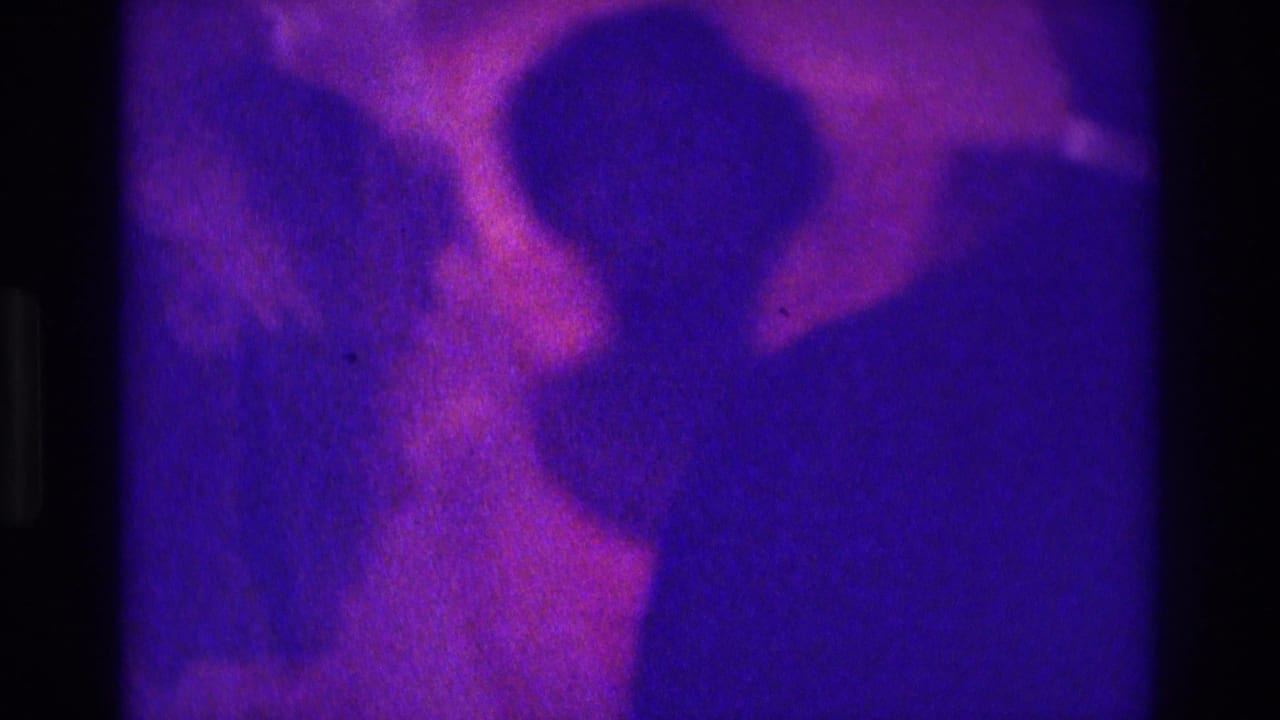1975 Atlanta 8mm frame with purple-magenta cast showing silhouetted wedding guests or party members in formal attire indoors.