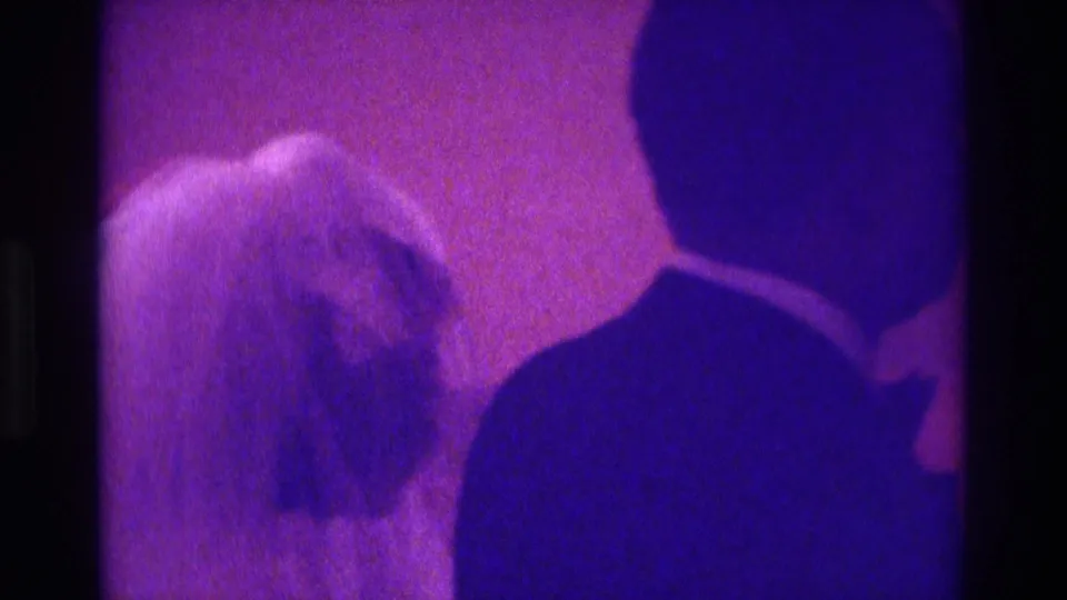 1975 Atlanta wedding home-movie frame showing a bride-like figure with light hair or veil near a dark-suited person indoors.