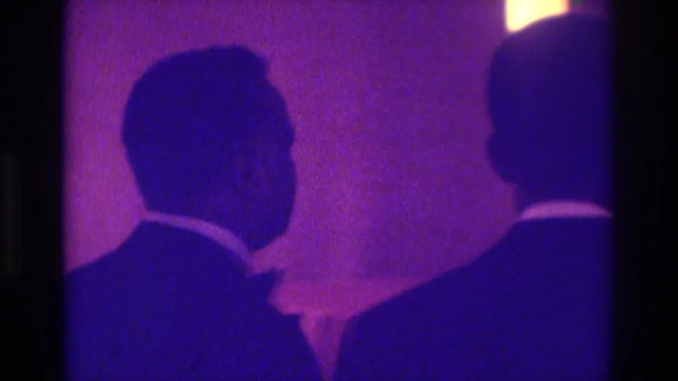 Purple-magenta 1975 Atlanta 8mm frame showing two dark-suited wedding guests or party members in profile and from behind.
