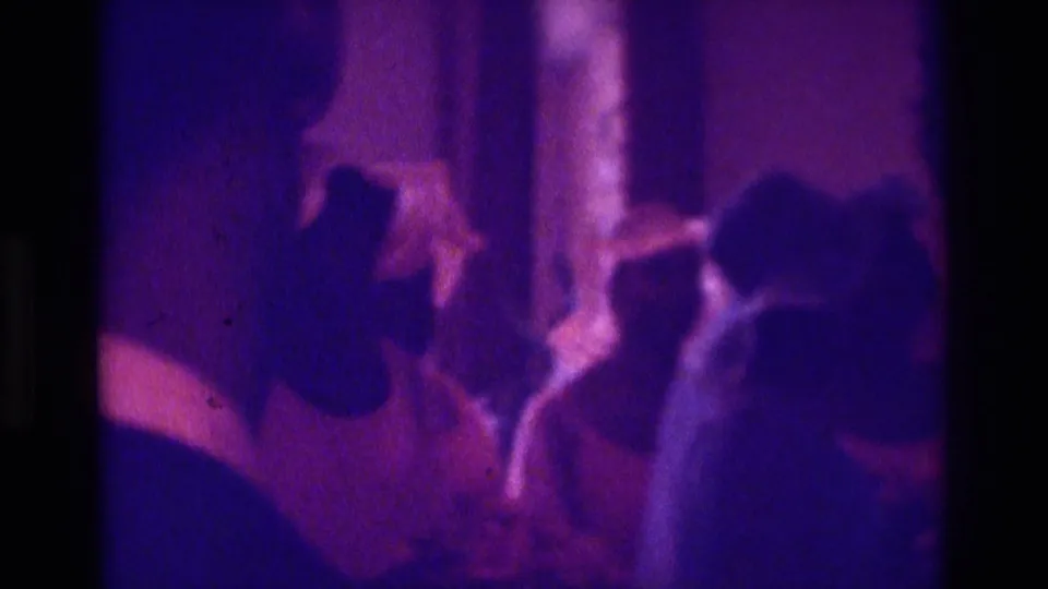 1975 Atlanta home-movie frame with side-profile silhouettes of attendees gathered inside a purple-lit ceremony space.