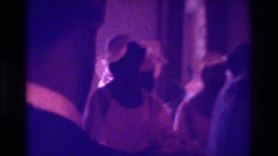 Atlanta 1975 frame showing foreground attendees and a robed figure during a likely wedding or baptism in a low-lit interior.