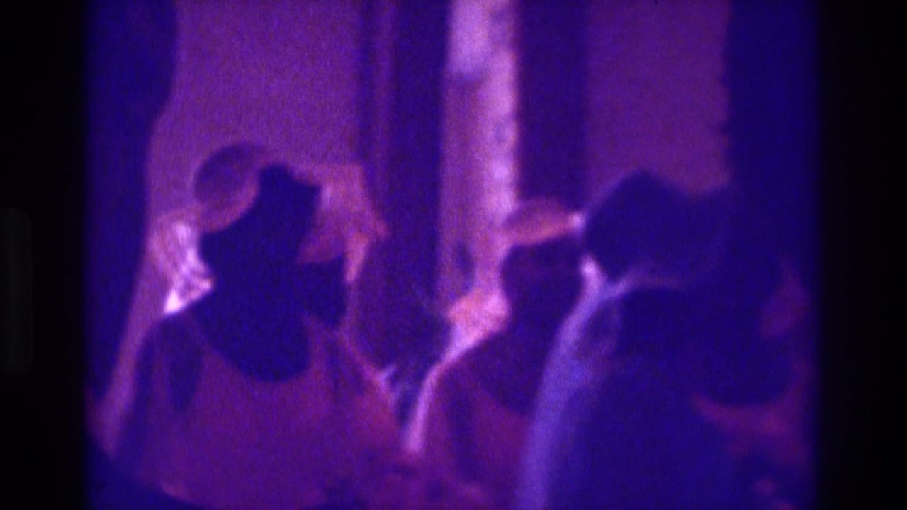 1975 Atlanta-area home-movie frame showing women in dress hats at a wedding or church ceremony under a strong purple color cast.