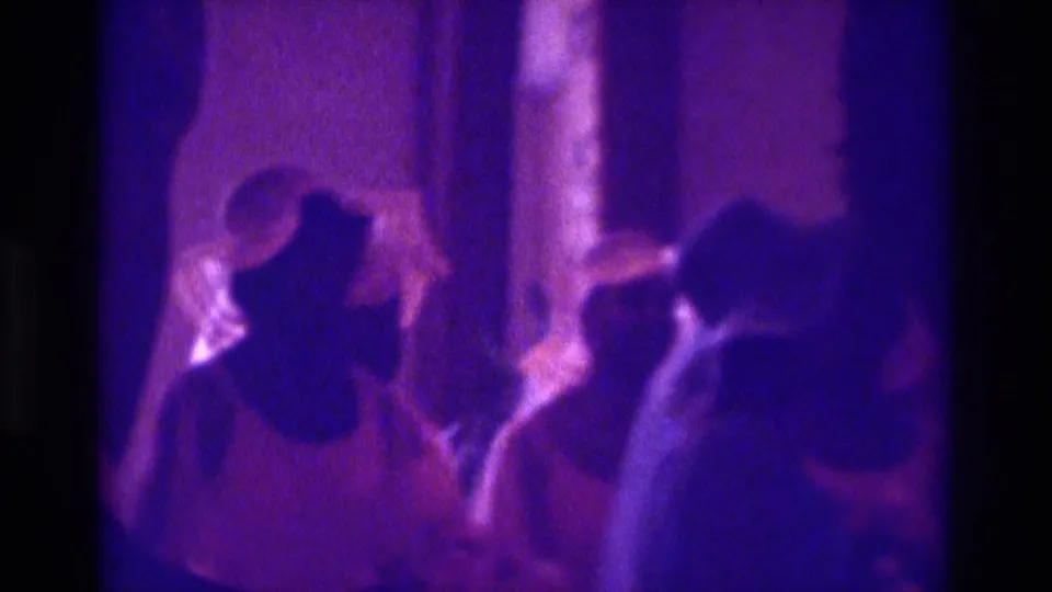 1975 Atlanta-area home-movie frame showing women in dress hats at a wedding or church ceremony under a strong purple color cast.