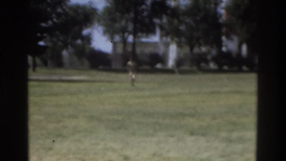 1975 Atlanta home-movie frame showing a distant runner on a lawn, seen through a dark window-like edge.