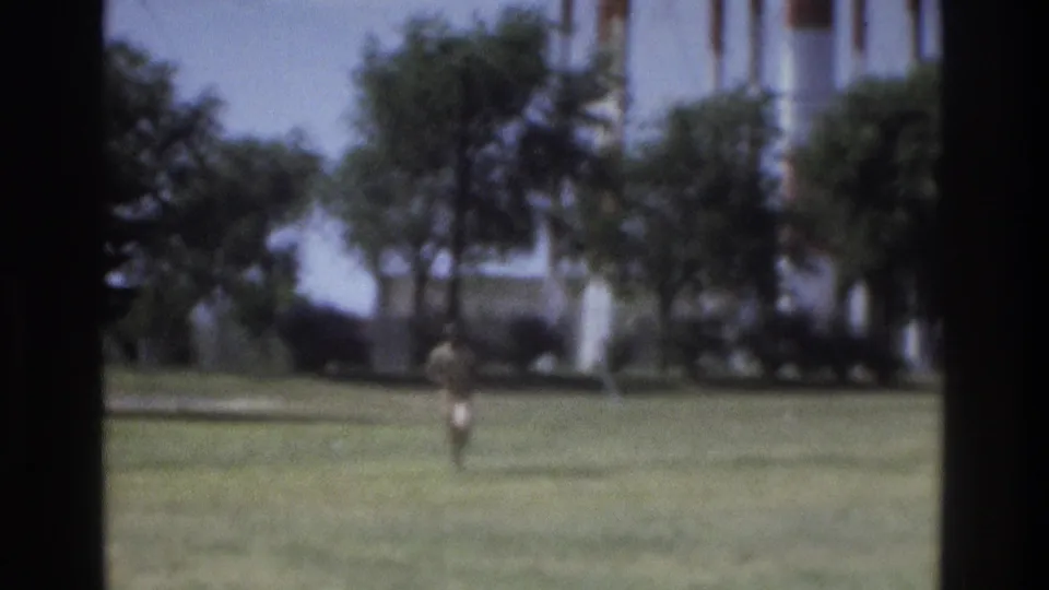 1975 Atlanta 8mm still showing a distant person running on a green field below trees and a pale background form.
