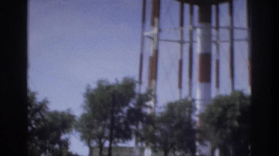 Final Atlanta home-movie frame showing a water tower structure above trees and grass under a clear sky.