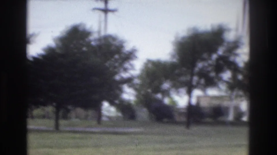 Soft 1975 Atlanta frame with grass, trees, a utility pole, and a light-toned structure glimpsed from a moving vehicle.