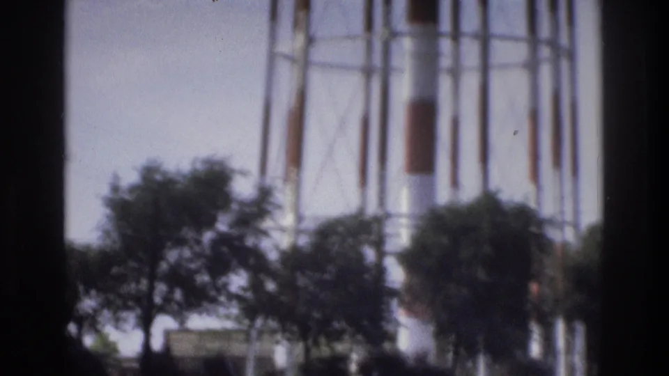 1975 Atlanta frame showing a red-and-white water tower partly obscured by trees and dark frame edges near a grassy roadside.