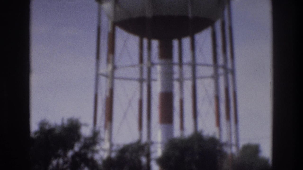 1975 Atlanta home-movie frame showing a tall elevated water tower structure rising above trees under a pale sky.