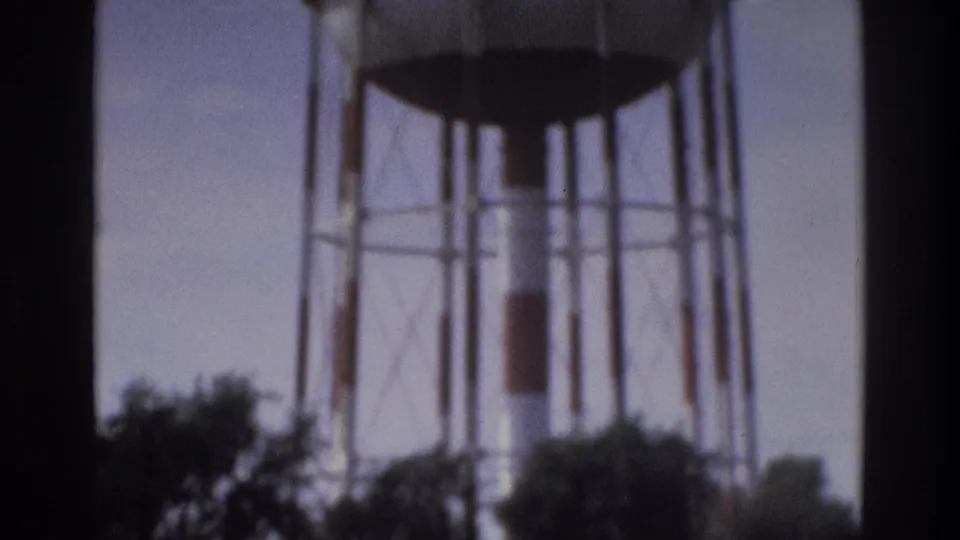1975 Atlanta home-movie frame showing a tall elevated water tower structure rising above trees under a pale sky.