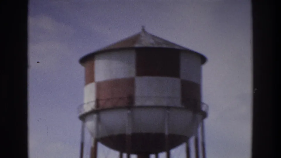 1975 Atlanta home-movie frame with a red-and-white checkered water tower on metal supports, framed softly against the sky.