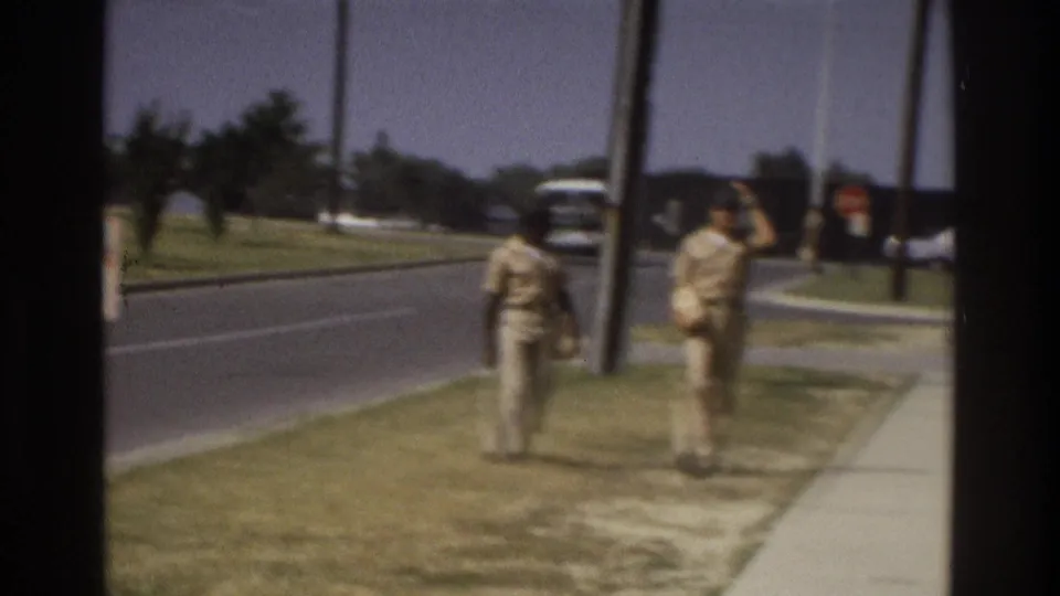 1975 Atlanta home-movie frame showing two pedestrians near the sidewalk below the red-and-white checkered water tower, with a road and distant vehicle in the background.