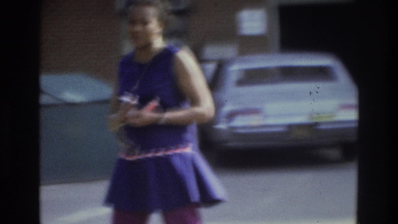 Woman in a purple sleeveless dress walks near parked cars.
