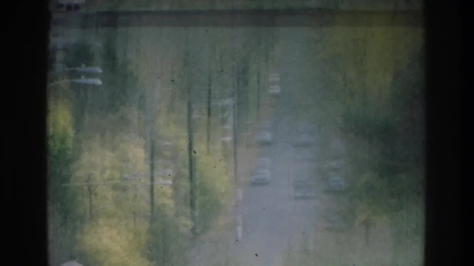1975 Atlanta 8mm view through dusty window panes toward a leafy hillside road with cars below.