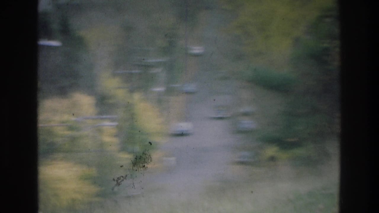 Atlanta-area 1975 home-movie view of a tree-lined road with slow traffic, seen through a dark window frame.