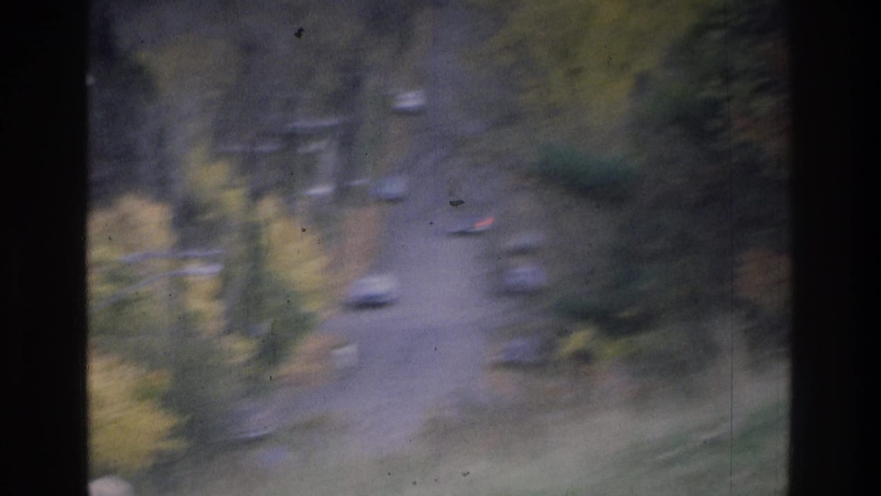 Distant cars on a curving road bordered by muted autumn trees.