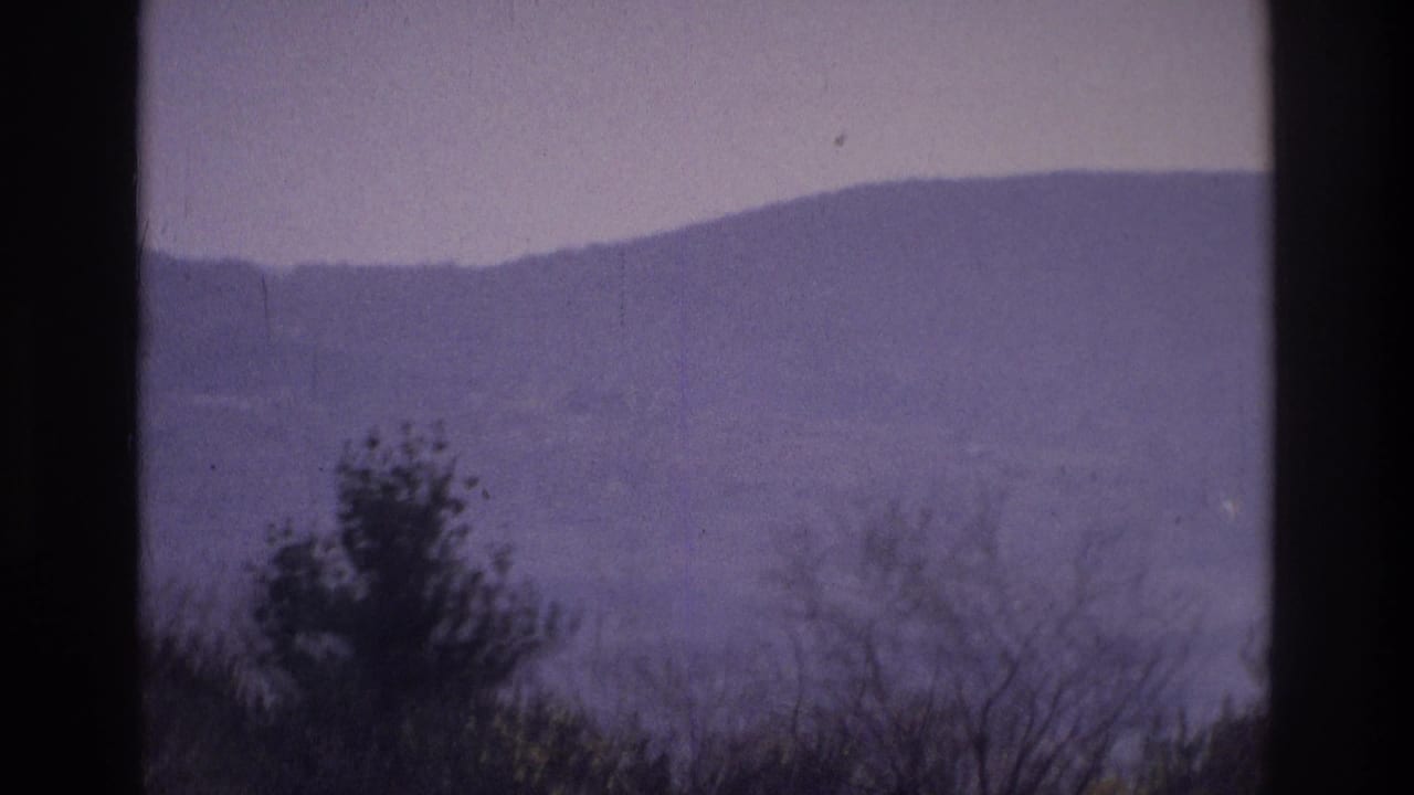 1975 8mm footage near Atlanta, Georgia, with layered hills, roadside trees, pale sky, and a dark vertical edge from the scan.