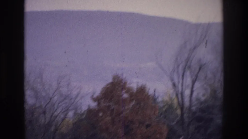 1975 8mm home-movie frame near Atlanta, Georgia, showing a hazy ridge over bare branches and muted autumn foliage.