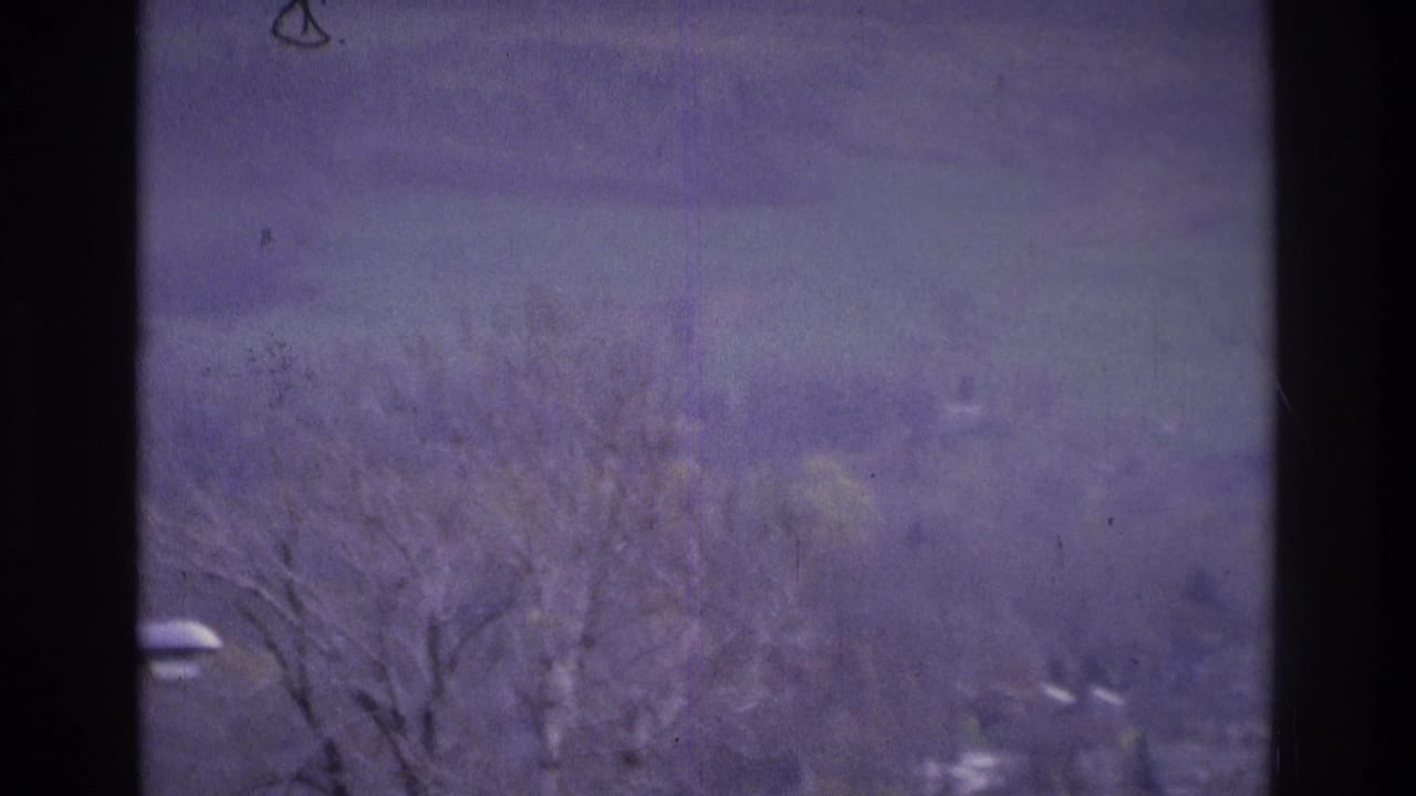1975 Atlanta home-movie frame showing a soft, purple-tinted distant suburban view with bare trees and scattered houses.