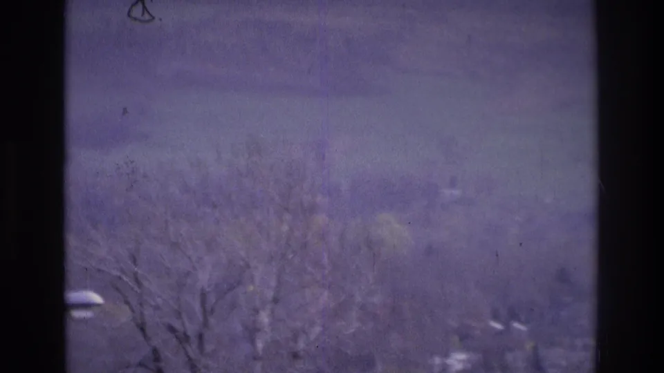 1975 Atlanta home-movie frame showing a soft, purple-tinted distant suburban view with bare trees and scattered houses.