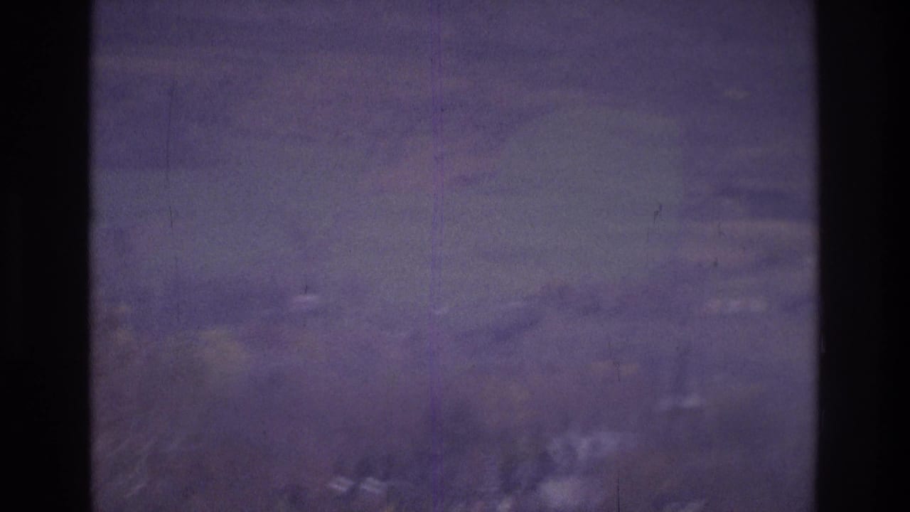 1975 Atlanta footage frame with distant hills, faint houses, cloudy sky, and a dark vertical film or gate artifact.