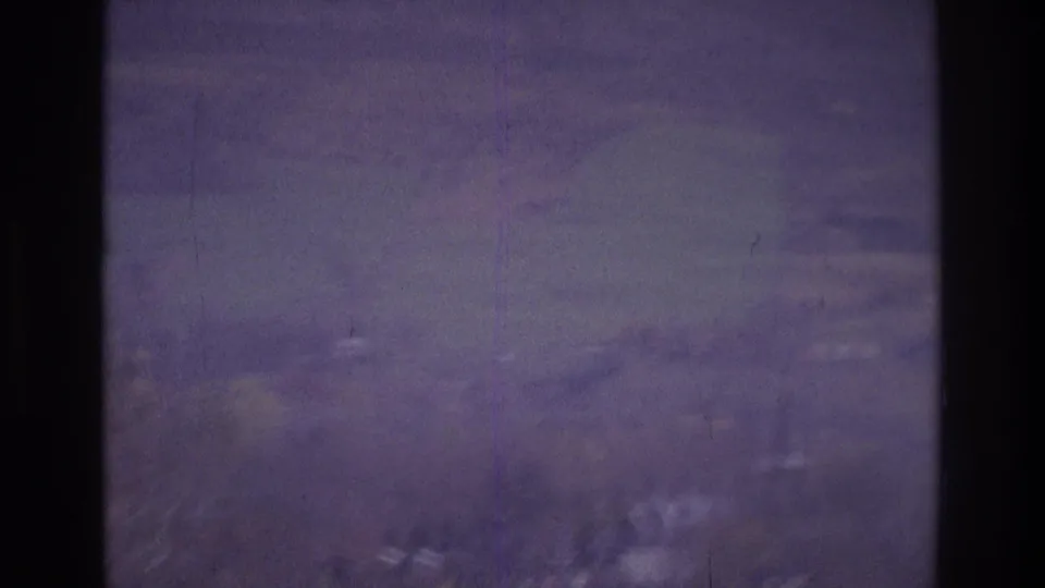 1975 Atlanta footage frame with distant hills, faint houses, cloudy sky, and a dark vertical film or gate artifact.