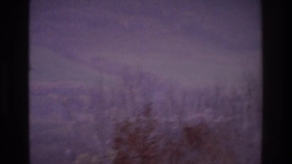 1975 Atlanta-area 8mm frame showing a hazy landscape through window glass, with bare trees and muted sky beyond the mullions.