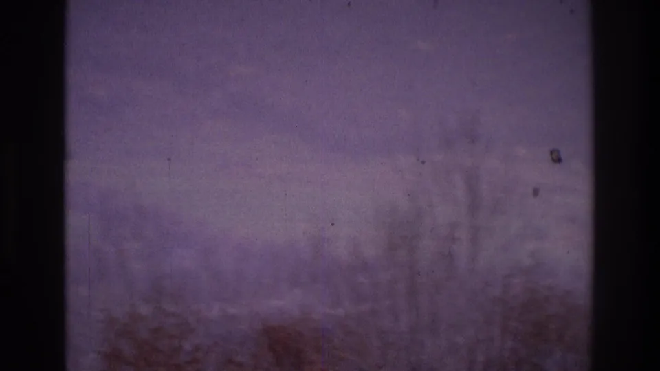 1975 Atlanta-area 8mm frame looking through a window at bare trees, haze, and a faint hillside settlement in the distance.