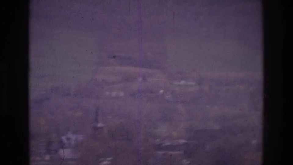 1975 Atlanta-area 8mm frame with a soft lower view of distant buildings and rolling ground through scratched, hazy glass.