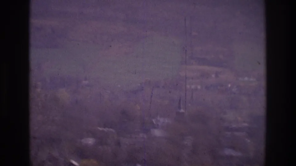 1975 Atlanta-area 8mm frame showing distant buildings and bare trees through a dark window frame and hazy glass.