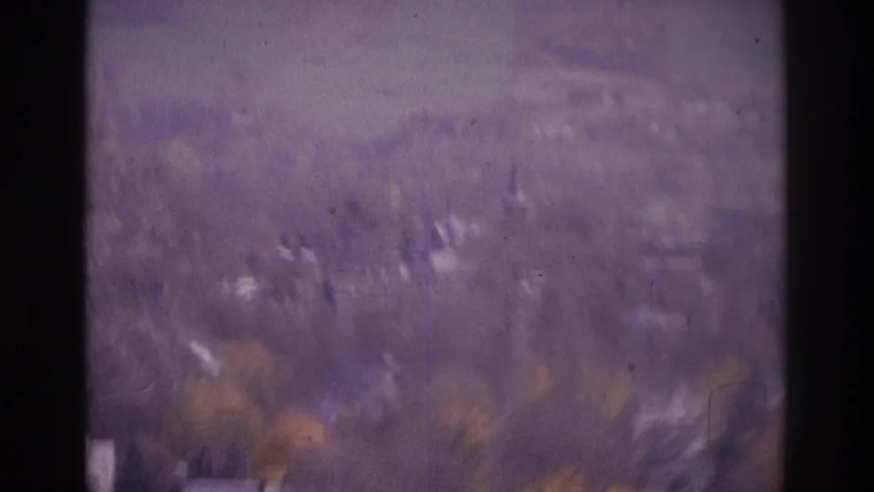 Soft 8mm frame showing a distant wooded residential area and rolling hills, with dark borders and purple color cast.
