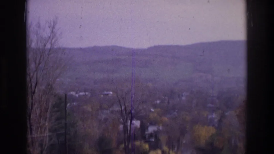 Atlanta-area 1975 8mm frame showing bare foreground trees, distant homes, rolling hills, and visible film wear.