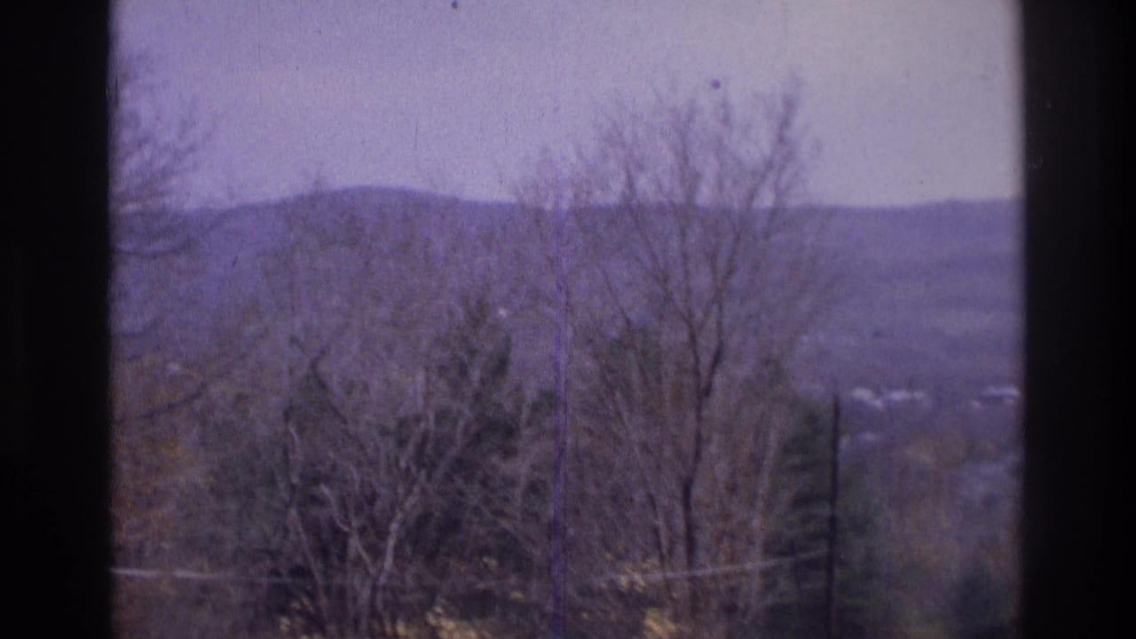 Atlanta-area 1975 home-movie frame with leafless trees, a hazy ridge, utility lines, and window borders.