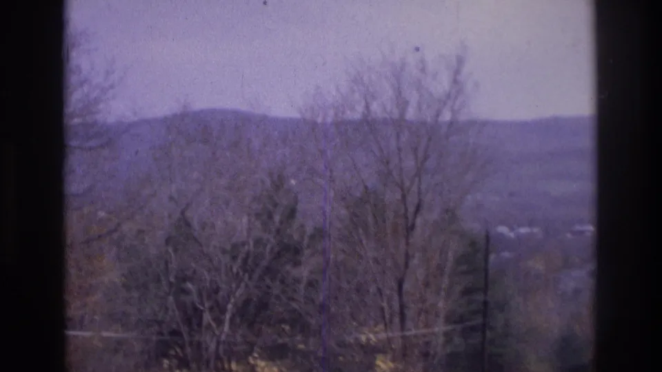 Atlanta-area 1975 home-movie frame with leafless trees, a hazy ridge, utility lines, and window borders.