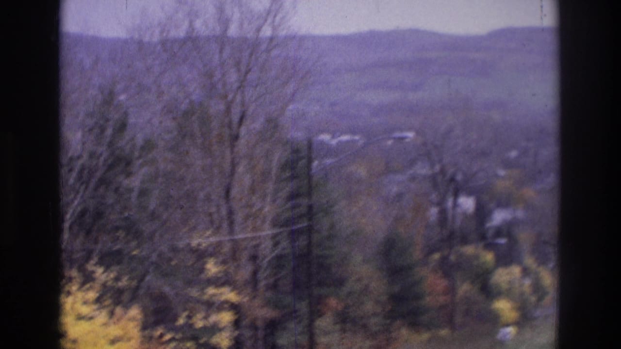 1975 Atlanta-area 8mm frame showing a hazy autumn hillside with bare trees, yellow leaves, utility poles, and distant homes.