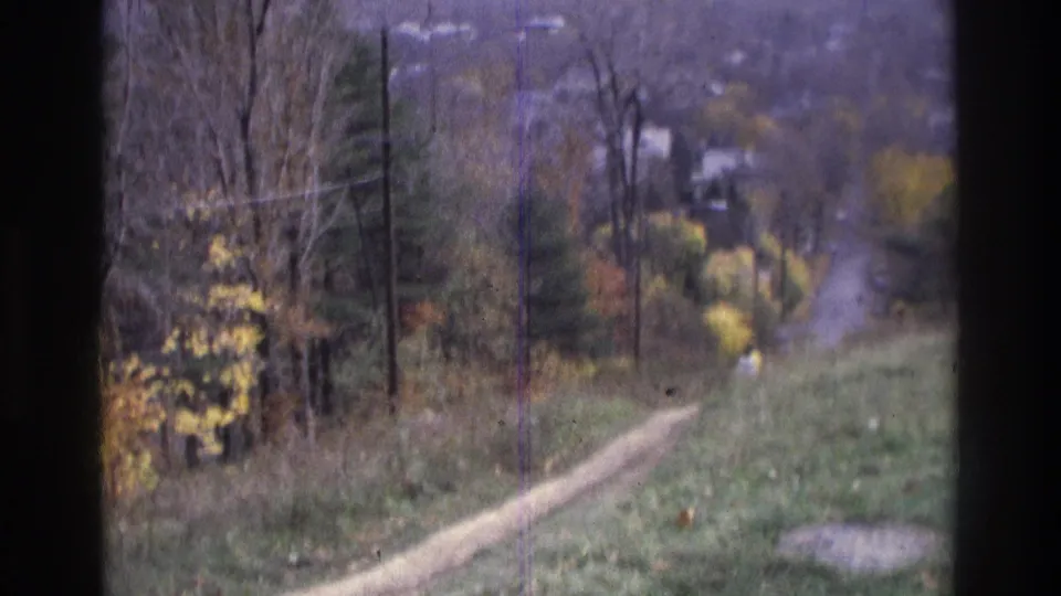 1975 Atlanta-area 8mm frame with a pale dirt path crossing a grassy hillside beside autumn trees and utility poles.