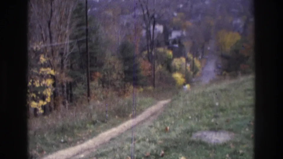 1975 Atlanta-area 8mm frame showing a winding dirt path, utility poles, autumn trees, and houses softened by distance and film grain.