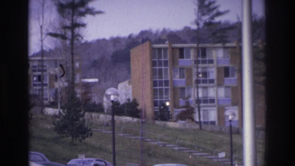 1975 Atlanta frame showing apartment buildings across a grassy slope, with trees, steps, lampposts, and wooded hills behind.
