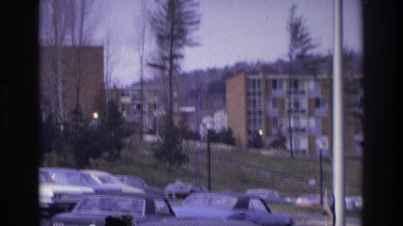 1975 Atlanta 8mm frame showing parked cars, trees, lampposts, and apartment buildings viewed through a window frame.