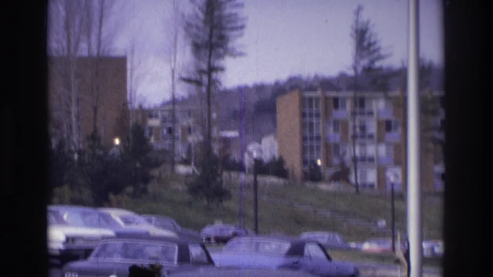 1975 Atlanta 8mm frame showing parked cars, trees, lampposts, and apartment buildings viewed through a window frame.