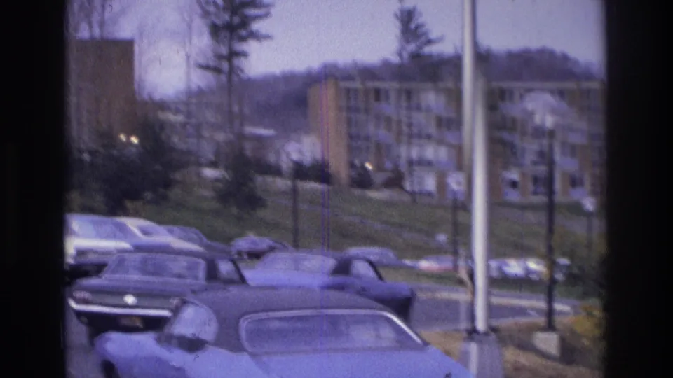 Soft 1975 Atlanta 8mm frame with classic cars in the foreground and apartment buildings rising behind trees.