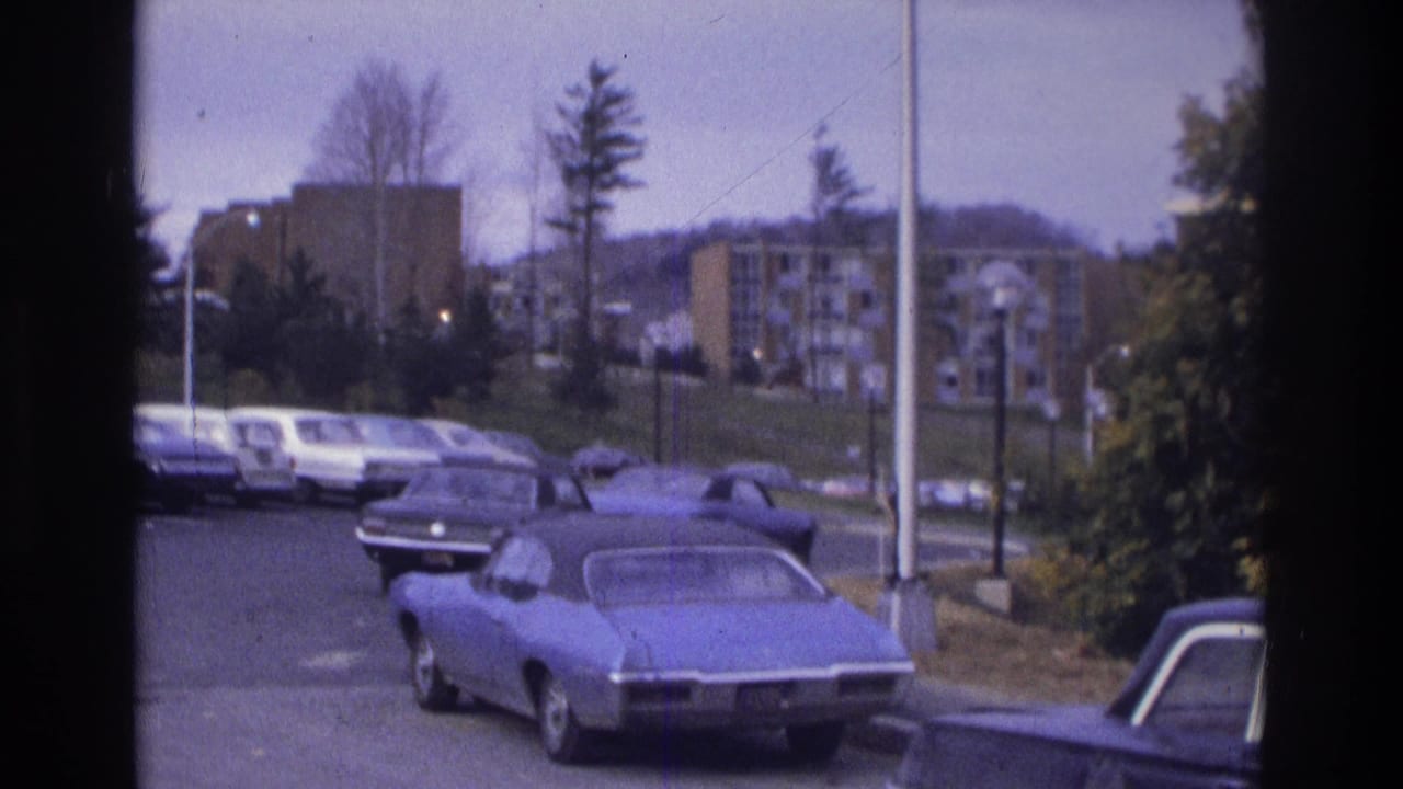 1975 Atlanta frame with a blue coupe prominent in the foreground and apartment buildings beyond a parking lot lined with cars.