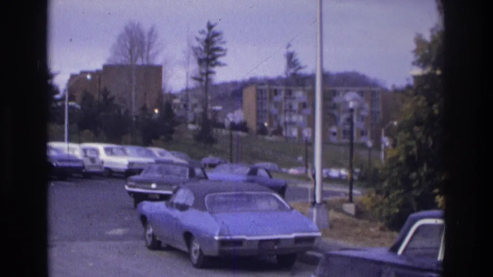 1975 Atlanta frame with a blue coupe prominent in the foreground and apartment buildings beyond a parking lot lined with cars.