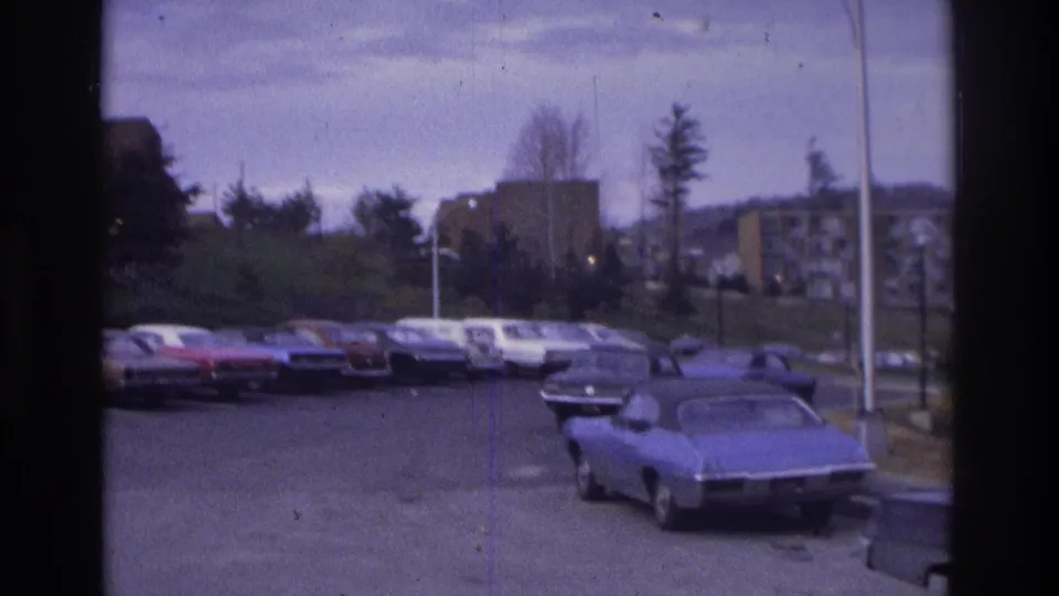 1975 Atlanta frame showing a wider suburban apartment parking lot with rows of period cars and a blue coupe at the right foreground.
