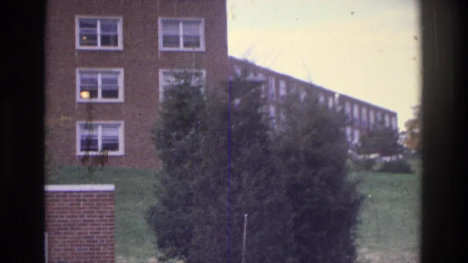 Atlanta 1975 8mm view of brick apartment buildings, a grassy slope, trees, and white-framed windows.