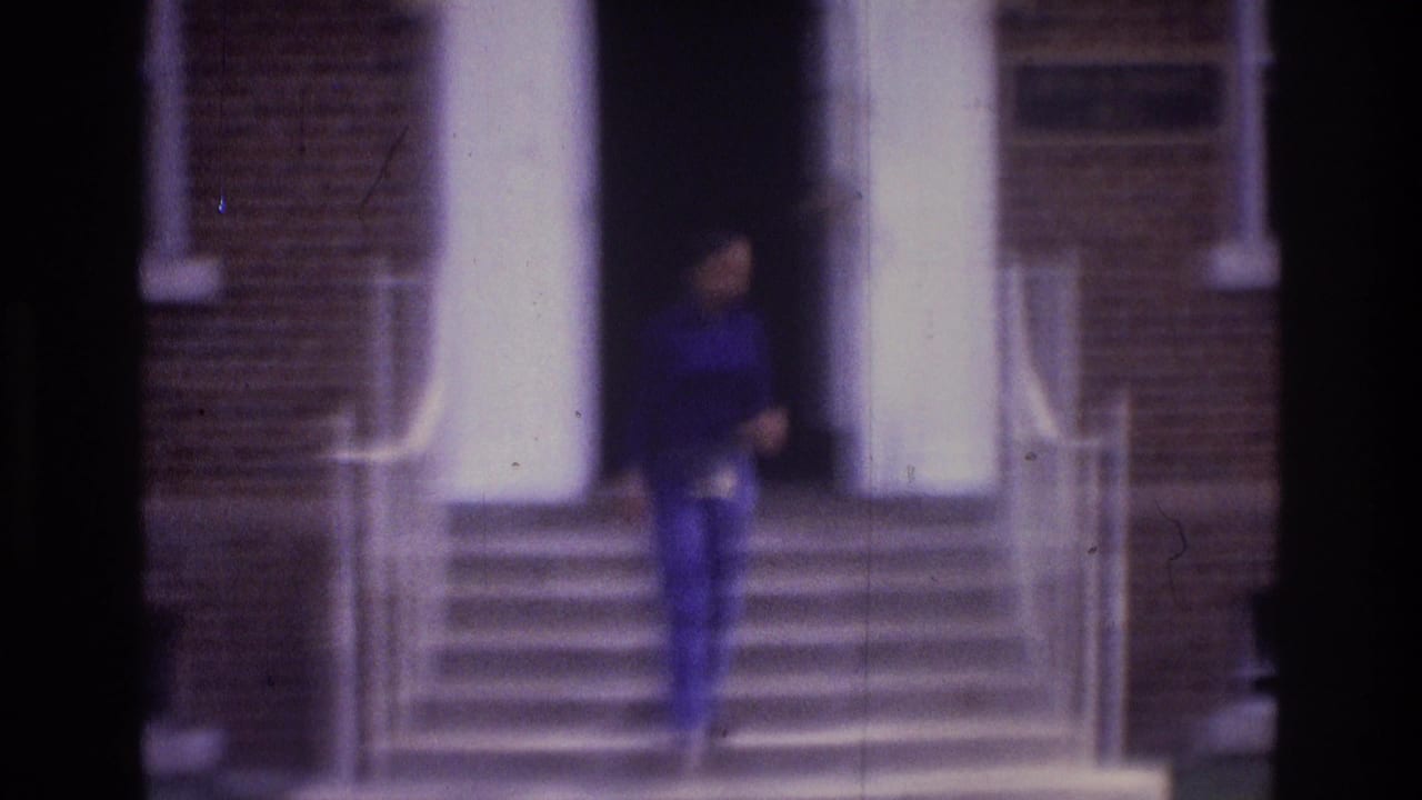 Soft 8mm frame from 1975 Atlanta showing a person at a brick building entrance with columns, handrails, steps, and wall lights.