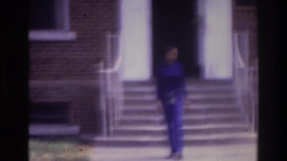 1975 Atlanta 8mm frame showing a person descending steps from a brick building entrance, with soft focus and purple color cast.