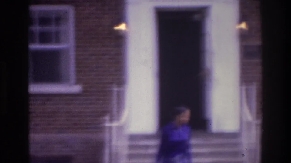 1975 Atlanta home-movie frame showing the person near the bottom of the steps beside a brick facade, white columns, and dark doorway.